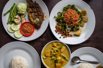Indonesian food: Kankung plecing (spicy water spinach dish), Ikan goreng (fried fish) and kare (curry) top view.