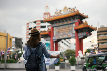 Young asian woman traveler with blue backpack and hipster hat looking map with tuk tuk Thailand background at China Town Bangkok. Traveling in Bangkok Thailand