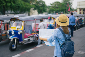 Young woman traveler with sky blue backpack and hat looking the map with tuk tuk Thailand background from china town Bangkok. Traveling in Bangkok Thailand. Travel concept