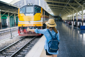 Young woman traveler with sky blue backpack and hat looking the map with train background at train station Bangkok. Traveling in Bangkok Thailand. Travel concept