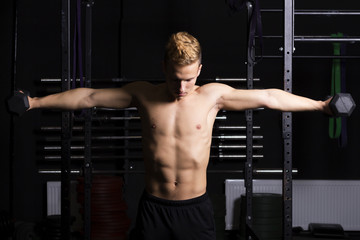 Fototapeta na wymiar Close Up portrait of a fit young man lifting weights in gym on dark background.