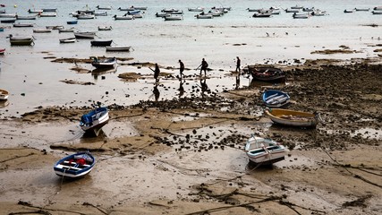 Atlantic Ocean scene during low tide with boats and silhouette of people in Cadiz, Andalusia, Spain.