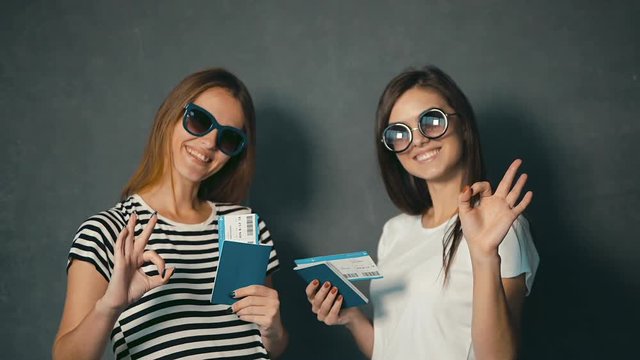 Happy female tourists showing tumbs up while holding the passports and tickets