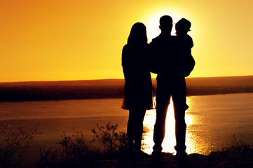 Family idyll. Silhouettes of mother, father and son standing together and admiring the sea during sunset in summer