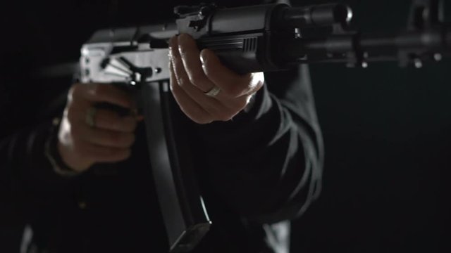 Armed man in black reloads an machine gun. Bandit with weapons in hand on a black background. The criminal scene. Hands with a gun close-up
