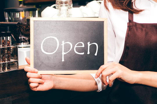 Barista holding chalkboard with word OPEN in coffee shop restaurant