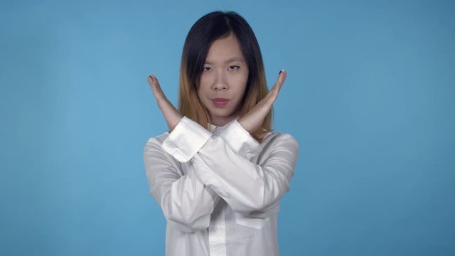 young asian woman posing showing hand gesture stopping refuse on blue background in studio. attractive millennial girl wearing white casual shirt looking at the camera