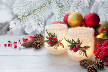 Fototapeta na wymiar Christmas decoration - decorated candles,red berries,cones and golden stars on white wooden table on background of tree branches in frost