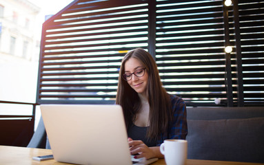 Young businesswoman with beautiful smile keyboarding on laptop computer, sitting in coffee shop....
