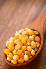 Yellow raw popcorn kernels on wooden spoon, photographed with natural light (Selective Focus, Focus one third into the kernels)