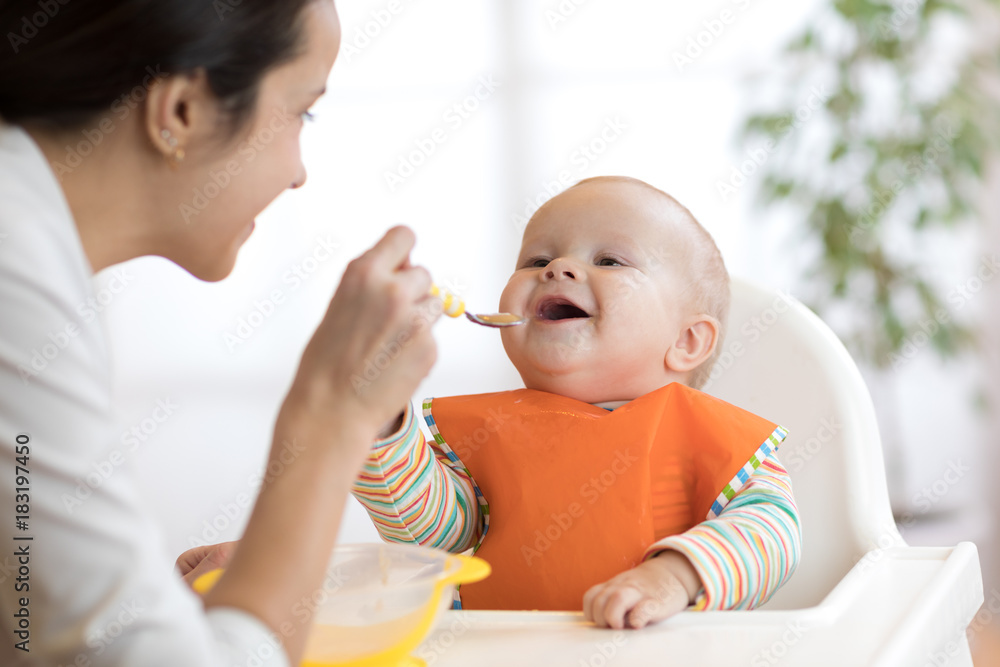 Wall mural mother feeding her baby with spoon. mother giving healthy food to her adorable child at home