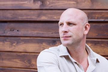 portrait of handsome bald man, on the wooden brawn backrgound. beige natural shirt. pring. summer. how weather, barbershop