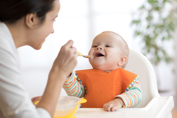 Mother feeding her baby with spoon. Mother giving healthy food to her adorable child at home - 183197450
