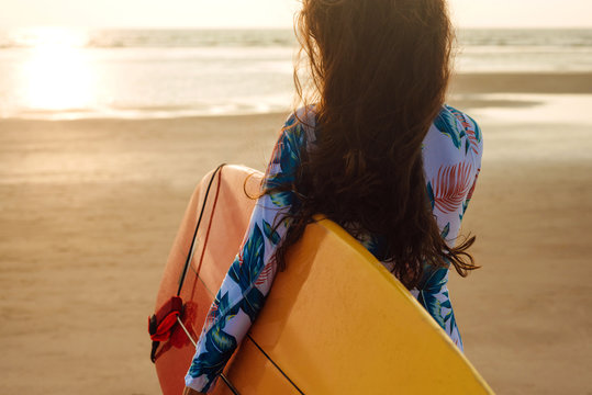Young surfer girl wearing swimsuit with long hear walking to the sea holding surfboard