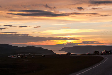 Fototapeta na wymiar A column of cars on a winding road at sunset, Mageroya island, Norway
