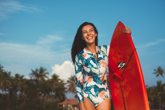 Young smiling surfer girl in swimsuit with long hear holding surfboard on the palm background