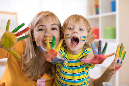 Smiling child boy and his mother having fun and showing hands painted in colorful paints