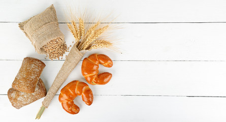 Bread products, ears of wheat, croissants, ciabatta on a white wooden background. Copy space.