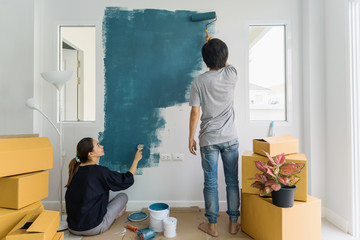 Obraz premium Young asian couple painting interior wall with paint roller in new house