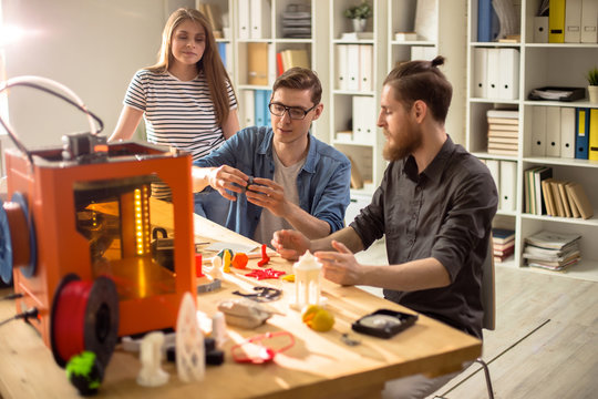Portrait of three young people using 3D printer working on creative design project together studying in college