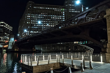 Chicago city riverwalk promenade at night with vintage drawbridge and illuminated Merchandise Mart building.