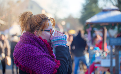 A woman is standing in a market in the winter drinking a cup of tea
