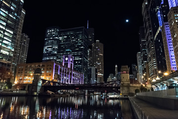 Fototapeta na wymiar Chicago city riverwalk promenade at night with vintage drawbridge, illuminated urban downtown buildings and the moon.