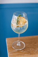 Cocktail in wine glass with dried slice pineapple and rosemary on the top.