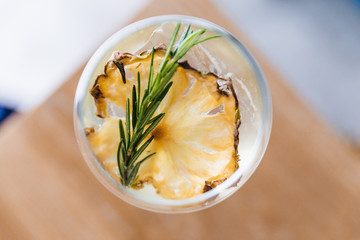 Top view of cocktail in wine glass with dried slice pineapple and rosemary on the top.