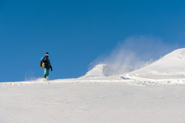 Naklejka na ściany i meble Freeride snowboarder rolls on a snow-covered slope leaving behind a snow powder against the blue sky