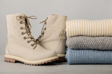 Leather women's light winter boots and a pile of knitted things (sweaters, scarves, gloves).