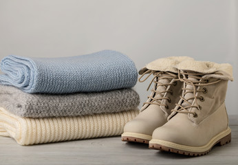 Leather women's light winter boots and a pile of knitted things (sweaters, scarves, gloves).