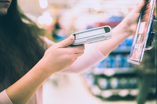 Pretty Young Brunette Woman Scanning Barcode On Some Product In Huge Supermarket By Hand Scanner (color Toned Image)