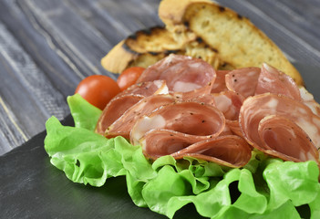 cold meat plate. Sliced ham with lettuce leaves on a dark stone background, selective focus