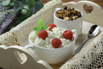 Homemade breakfast: cottage cheese with fresh raspberries and granola. In a white porcelain bowl, on a wooden tray