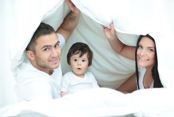 Happy family posing under a duvet while looking at the camera