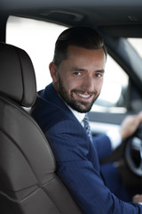 Handsome young man sitting in the front seat of a car looking at the camera