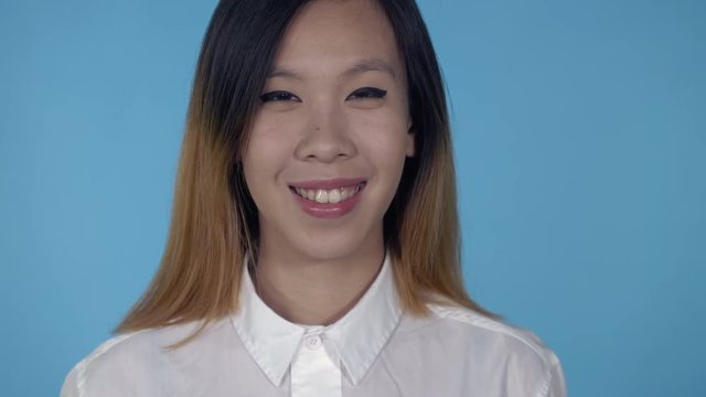 close up portrait young asian woman laughing on blue background in studio. attractive millennial girl looking at the camera