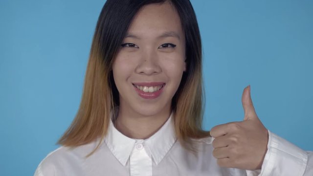 close up portrait young asian woman laughing shows sign like on blue background in studio. attractive millennial girl looking at the camera laughing