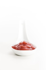 Creamy red sauce in white ceramic spoon, on white background.