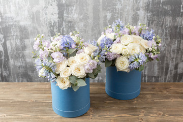 two flower bouquet in a hat box blue. standing on a wooden table. On the background old gray wall art. copy space.