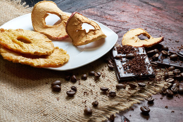Coffee, chocolate and dried fruits on wood background with linen