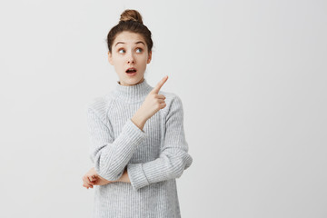 Teenage girl with wonder looking to side and showing with index finger. Curious female employee...