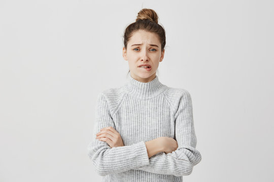 Puzzled woman wearing casual clothes standing with arms crossed looking at camera. Female illustrator biting lips with feelings of regrets about work. Emotions concept