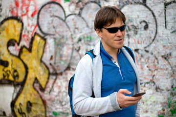 Obraz premium Middle aged man outdoor using smartphone against wall. Urban lifestyle, internet and gadget dependence, social network concept.