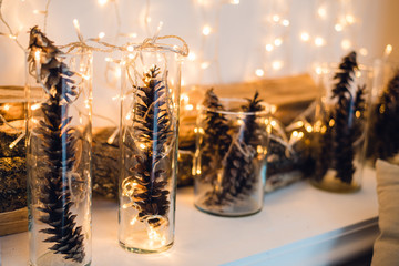 Christmas or New Year composition with garlands in small glass candlesticks and pine cones, wooden bars on a background, festive evening, selective focus