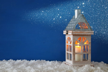Wooden old house with candle over the snow and blue background.