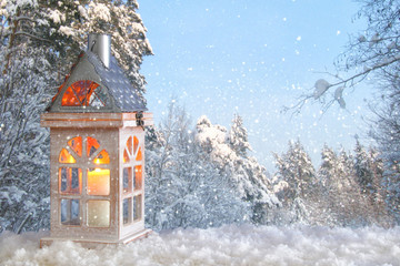Naklejka premium Wooden old house with candle over the snow and blurry magical winter landscape background.