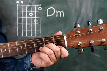 Man in a blue denim shirt playing guitar chords displayed on a blackboard, Chord Dm