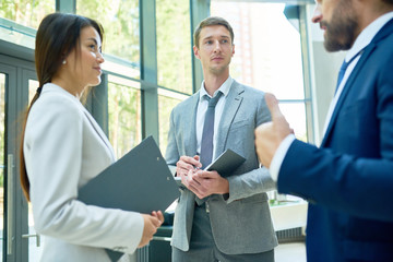 Group of successful businesspeople holding clipboards standing in hall of modern office building discussing work with boss, focus on smiling Asian businesswoman